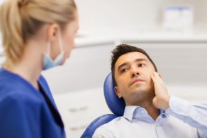 a dental patient during an appointment in pain, talking to his oral surgeon about a wisdom tooth extraction