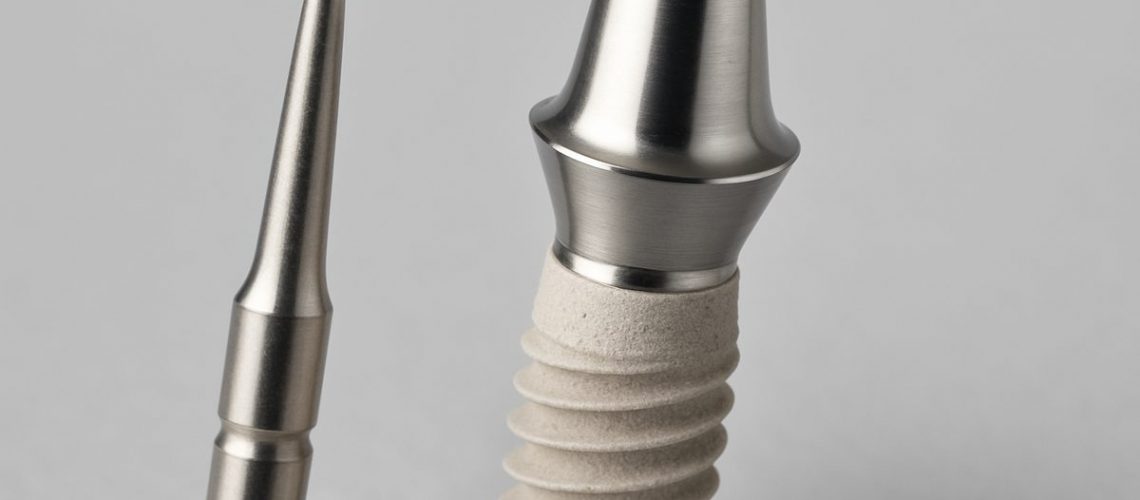 Image of a close-up showcasing a dental implant, highlighting its coating and abutment, next to a surgical tool. No text on image.